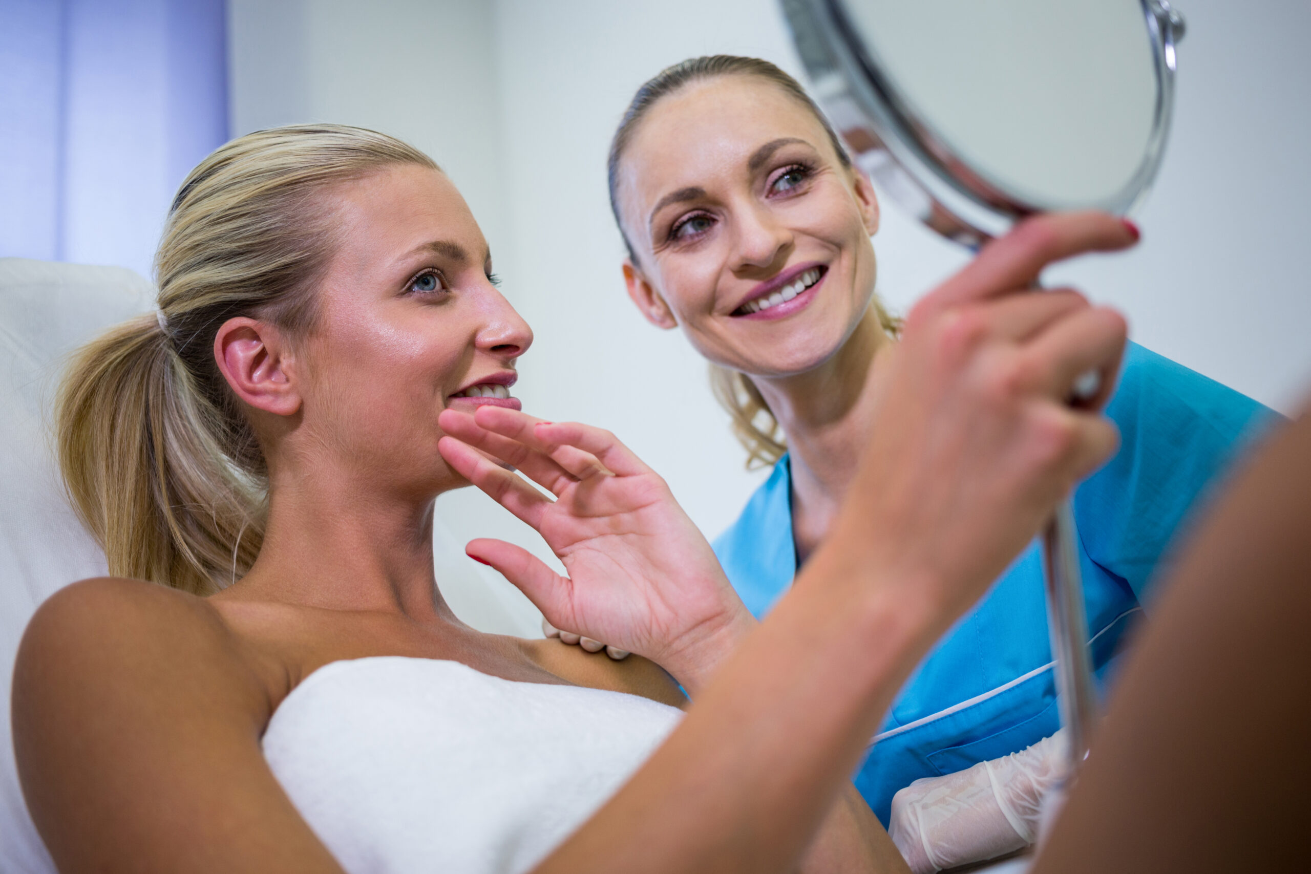 Happy woman checking her skin in the mirror after receiving cosmetic treatment